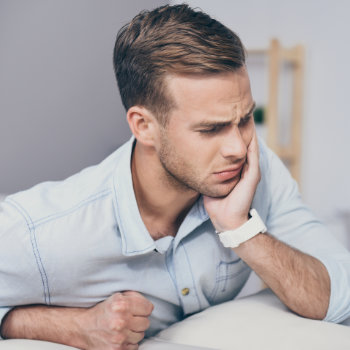 man holds his cheek with pain