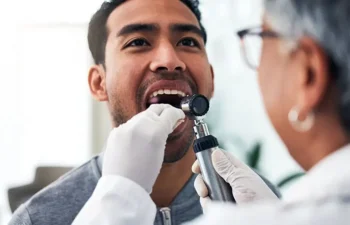 A healthcare professional examines a man’s throat with a medical instrument while he opens his mouth.
