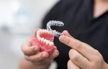 A person holds a dental model in one hand and a clear aligner in the other, demonstrating how the aligner fits over the teeth.